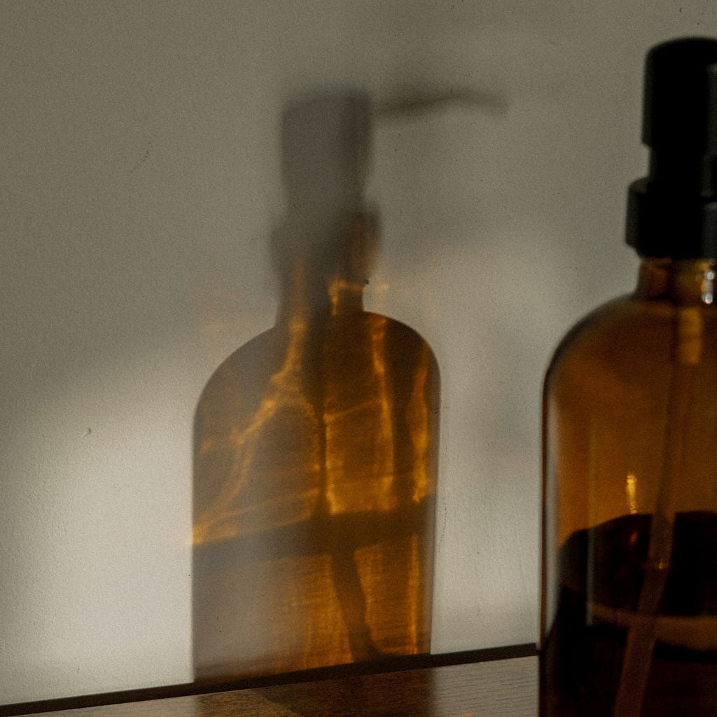 Brown glass skincare bottle with a black cap on a reflective surface, from LADA Beauty serving El Paso, TX